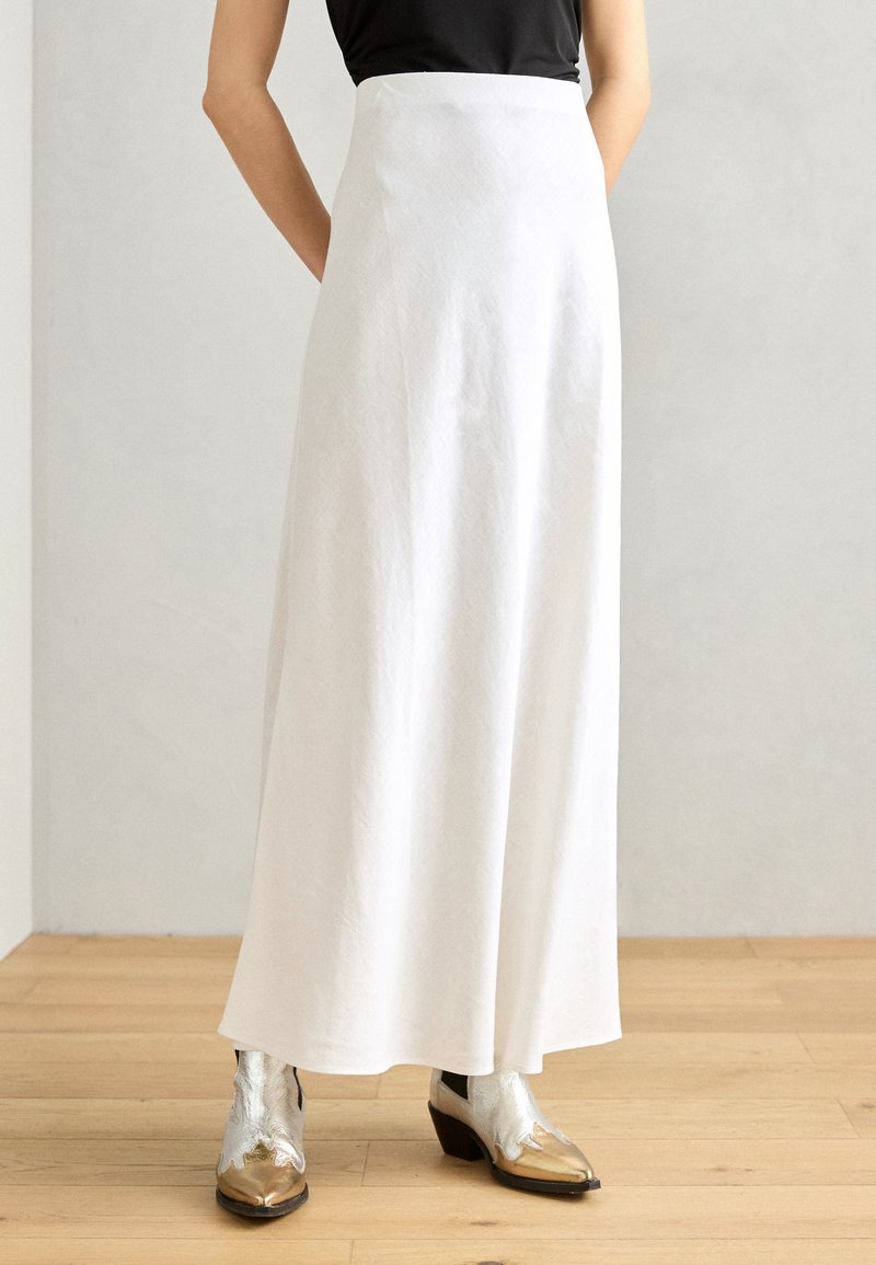 White long skirt with a high waist, crafted from textured fabric, paired with silver and gold ankle boots with a distinctive design.