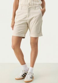 Beiga bomullsshorts med uppvikta ben, slät front och sidofickor. Matchas med grå sneakers med svarta ränder och vita strumpor.