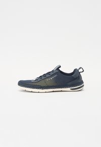 Zapatilla deportiva de malla en color marino con acentos grises, suela blanca y detalles de logo; presenta un diseño con cordones y un upper texturizado para mayor transpirabilidad.