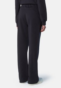 Pantalones de chándal azul marino oscuro hechos de una suave mezcla de algodón, con un diseño de pierna ancha, cinturilla elástica y ligeras aberturas laterales en los tobillos.