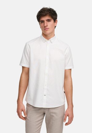 Camisa blanca de botones de manga corta hecha de tejido ligero. Presenta un cuello clásico y un corte recto, combinada con pantalones gris claro.