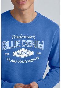 Sudadera azul de algodón con cuello redondo. Presenta texto blanco que incluye "BLUE DENIM," "BLEND" y "CLAIM YOUR RIGHTS."