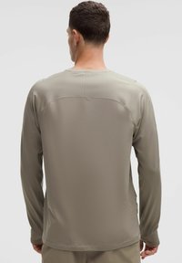 Căma�șă cu mânecă lungă în nuanță de taupe deschis, textură netedă, cusături plate, decolteu tip crew și design ajustat. Fără logo-uri sau modele vizibile.