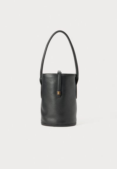 Bolso cubo de cuero negro con textura suave, forma cilíndrica, asa corta y un acento de hardware en tono dorado en la parte frontal.