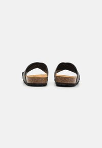 Sorte sandaler med åpen bak, korkfotbed og teksturert såle. Har et enkelt design med buede remmer og matt finish.