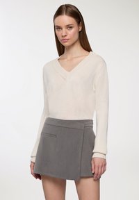 Kremowy sweter z dekoltem w serek i długimi rękawami, w po�łączeniu z szarym spódnicą typu wrap, która ma boczną kieszeń, wykonaną z tkaniny o fakturze.