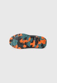 Schuhsohle mit robustem Profil in orange, blaugrün und schwarzem Camouflage auf einem schlichten weißen Hintergrund.