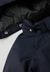 Marineblå overtøj med en struktureret overflade, der har en quilted sort foring, trykknaplukninger og et højt kravedesign.