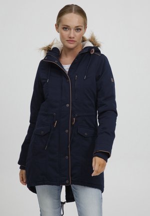 Marinblå parka-jacka med foder av konstpäls, framdragkedja och tryckknappar, samt två fickor med lock. Har kontrasterande bruna detaljer.