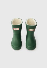 Botas de borracha verdes com sola texturizada, forro branco macio e logótipo HUNTER vermelho na parte da frente, apresentando um design arredondado.