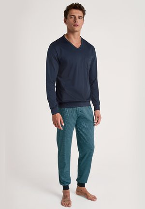 Marineblaue Langarm-V-Ausschnitt-Bluse mit einer frontalen Tasche, kombiniert mit türkisfarbenen gemusterten Jogginghosen, die elastische Bündchen und einen Kordelzug an der Taille haben.