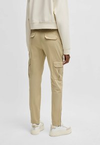 Pantaloni cargo beige con tasche laterali, dettaglio con zip alla caviglia e una vestibilità rilassata. Abbinati a scarpe da ginnastica bianche e una felpa color crema.