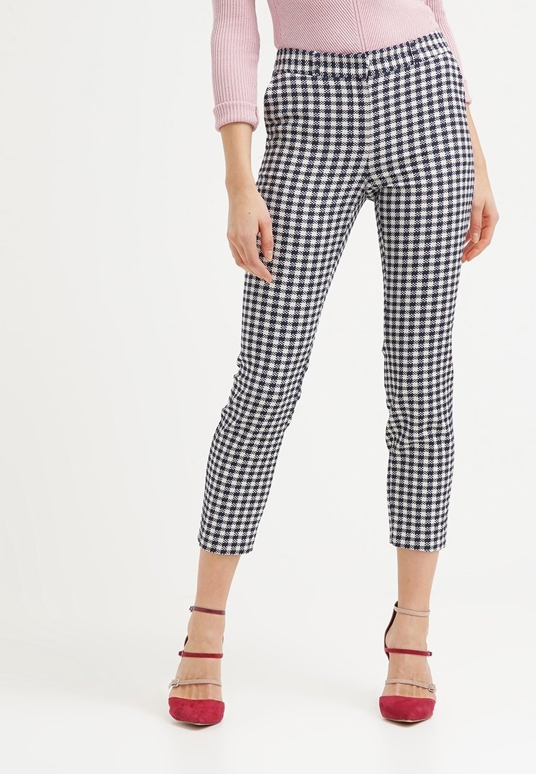 Black and white houndstooth patterned fitted pants with a high waist and cropped length, paired with red block-heeled shoes.