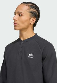Black, textured long-sleeve shirt with a henley collar, featuring three buttons and a white Adidas logo on the left chest.