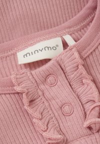 Lys pink ribbet beklædning med flæse detaljer, prydet med to runde plastikknapper og et mærketik. Blød stoftekstur.