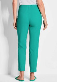 Pantalons verts à taille élastique avec une jambe droite, fabriqués dans un tissu léger. Ils présentent une texture lisse et des poignets de cheville ourlés.