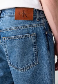 Lichtblauwe denim jeans met een bruine leren Calvin Klein-label op de achterkant van de tailleband en een achterzak met contrasterende stiksels.