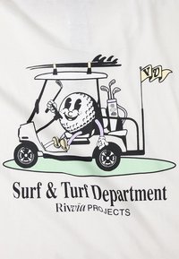 Maglietta bianca con un personaggio di pallina da golf in stile cartone animato che guida un carrello da golf con mazze, testo "Surf & Turf Department" e accenti verdi.