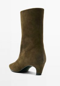 Stivaletto alla caviglia in camoscio marrone con punta appuntita e tacco medio rastremato. Texture liscia e silhouette elegante.