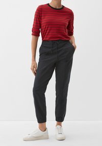 Chemise à manches longues rayée rouge avec encolure noire, associée à un pantalon de jogging noir à taille élastique. Modèle portant des baskets blanches.