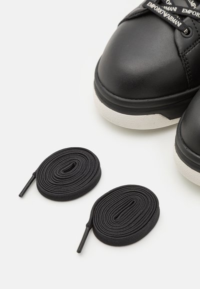 Black leather sneakers with white rubber soles, featuring black laces laid out in loops alongside the shoes.