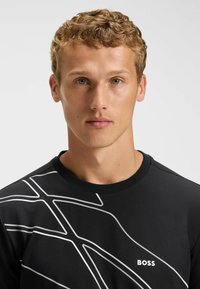 Sort sweatshirts med hvide grafiske linjer og "BOSS" logo i hvidt. Rund halsudskæring og blødt stof med glat tekstur.