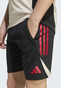 Schwarze Sportshorts mit roten Adidas-Streifen und Logo. Hergestellt aus leichtem Material, mit seitlichen Taschen und einem kontrastierenden beigen Panel.