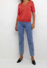 Coral v-neck sweater, short sleeves, paired with light blue straight-leg jeans and black pointed-toe heels. Smooth fabric, casual design.