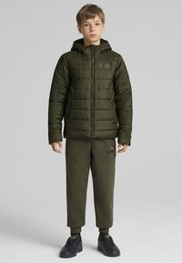 Oliven grøn pufferjakke med lynlås, strukturerede paneler og hætte, parret med matchende joggers og sorte sneakers.