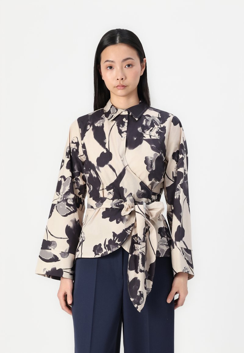 Blusa crema con motivo floreale scuro, con colletto, cintrata in vita, caratterizzata da maniche lunghe e larghe e una texture liscia.