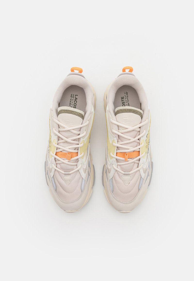 Scarpe da ginnastica color beige chiaro realizzate con materiali misti, inclusi mesh e suede. Accenti in giallo pastello e arancione, con una suola testurizzata.