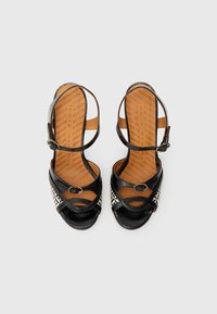 Μαύρα δερμάτινα σανδάλια με ψηλό τακούνι, με λουράκι στον αστράγαλο, διασταυρούμενο σχέδιο και γεωμετρικό λευκό μοτίβο στην εξωτερική λωρίδα. Καφέ επενδεδυμένη ανατομική σόλα.