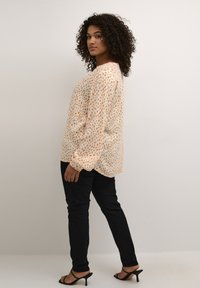 Long-sleeve blouse in light orange with a pattern of small, abstract speckles. Paired with black skinny jeans and black heeled sandals.
