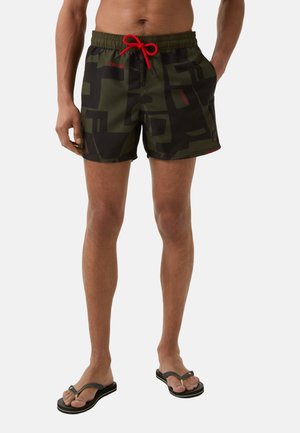 Zwemshorts in een camouflage groen en zwart patroon, met een rode trekkoord, zijzakken en een korte binnenbeenlengte. Rubber slippers zijn te zien.