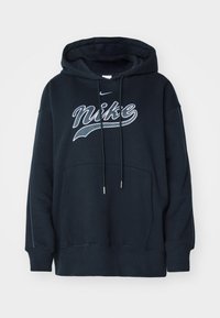 Svart luvtröja med stor vit Nike-logotyp, dragsko med metallspetsar och en framficka. Har ribbad nederkant och muddar.