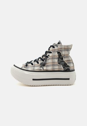 Magas szárú sneaker fehér platform talppal, bézs kockás szövet felsőrész, fekete fűzőkkel és kopott lyukakkal, amelyek alatt fekete csipke látható.