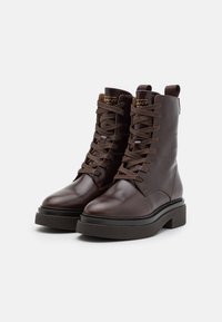 Brown leather ankle boots with a rounded toe, flat rubber sole, and lace-up design; features a stitched detail and pull tab on the back.