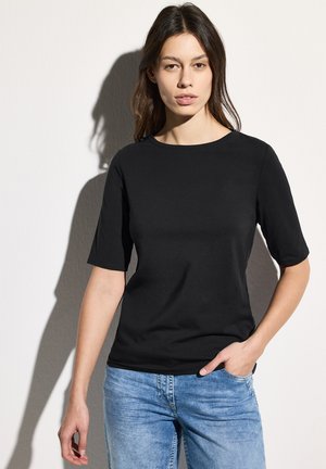 T-shirt noir à manches courtes avec un col rond, fabriqué à partir d'un tissu doux. Porté avec un jean en denim bleu clair, présentant une coupe décontractée.