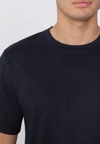 Tmavě modré tričko s kulatým výstřihem, krátkými rukávy a hladkou, elastickou, žebrovanou texturou. Minimalistický design bez vzorů nebo akcentů.
