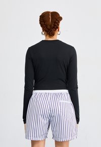 Svart langermet skjorte med en tettsittende design sammen med hvite shorts med vertikale lilla striper og elastisk liv.