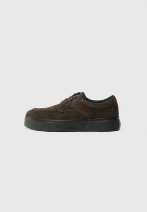 Brown suede sneaker with a low profile, round toe, lace-up design, textured black rubber sole, and minimal branding.