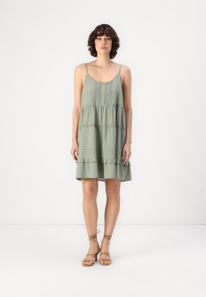 Vestido verde sin mangas con un diseño en capas, que presenta volantes en el dobladillo y detalles texturizados en el cuerpo. Color sólido con un corte holgado.