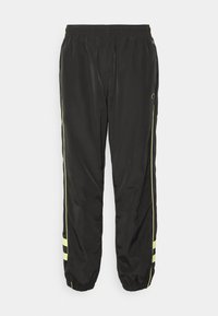 Svarta träningsbyxor med elastisk midja, med gula sidosträck och en strukturerad yta. Muddar som är samlade för en smalare passform.