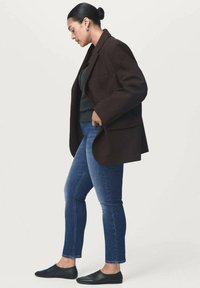 Brun oversized kavaj, grå tröja, blå jeans, svarta slip-on skor. Kavajen har en strukturerad design och framträdande slag.