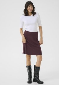 Jupe bordeaux mi-longue Marl avec une taille cintrée, associée à un haut blanc à manches courtes à côtes et des bottes noires montantes.