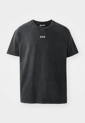 Dunkelgraues Baumwoll-T-Shirt mit Rundhalsausschnitt und kurzen Ärmeln, versehen mit einem kleinen Etikett-Detail auf der Brust. Weiche Textur.