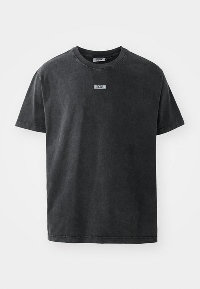 T-shirt de algodão cinza escuro com gola redonda e mangas curtas, apresentando um pequeno rótulo decorativo no peito. Textura suave.