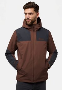 Bruine en marineblauwe outdoorjas met een ritssluiting aan de voorkant en capuchon, met een gladde textuur en contrasterende kleurvlakken op de schouders en mouwen.