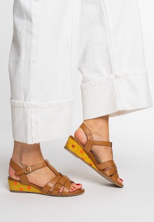 Braune Ledersandalen mit überkreuzten Riemen und einem Keilabsatz mit gelber Basis, die mit roten Punkten verziert ist.
