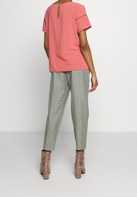 Top rosa a maniche corte con uno scollo a chiave sul retro, abbinato a pantaloni a quadri verde chiaro e stivaletti alla caviglia in stampa pitone marrone.